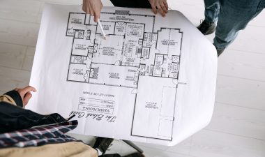 pexels photo 8962803 8962803 Two architects examining a detailed floor plan blueprint on a table indoors.